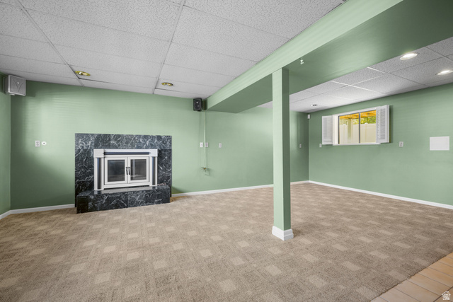 2088 Falcon Way Sandy, UT 84093 - Photo 32 of 46 Spacious room featuring a dark stone fireplace with a glass enclosure, patterned carpet, light green walls, a drop ceiling with recessed lighting, and a window with white louvered shutters