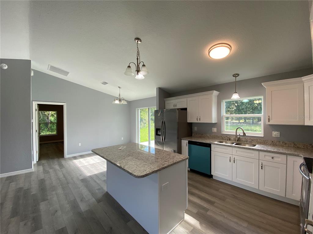 2827 Southwest 140th Loop Ocala, FL 34473 - Photo 7 of 29 a kitchen with granite countertop a stove a sink a refrigerator and white cabinets with wooden floor