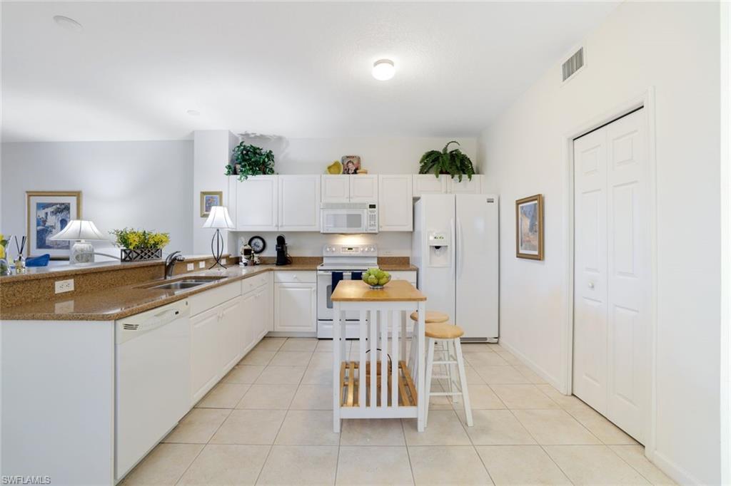10049 Heather Lane, Unit 101 Naples, FL 34119 - Photo 13 of 28 Kitchen with white appliances, white cabinets, light tile patterned flooring, and dark stone countertops