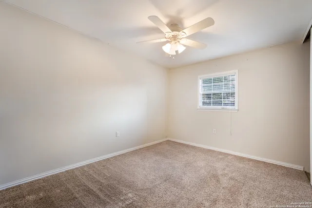 an empty room with a chandelier fan and windows