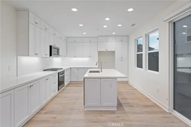 a large white kitchen with wooden floors and stainless steel appliances