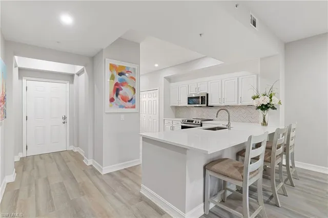 a kitchen with stainless steel appliances a sink a stove a refrigerator with white cabinets and wooden floor