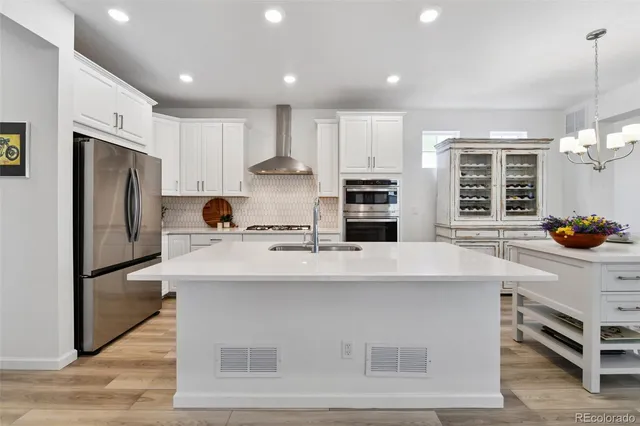 a kitchen with stainless steel appliances kitchen island granite countertop a stove a sink a refrigerator and white cabinets with wooden floor