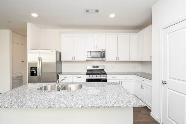 a kitchen with stainless steel appliances granite countertop a refrigerator a sink dishwasher a stove and white countertops with wooden floor