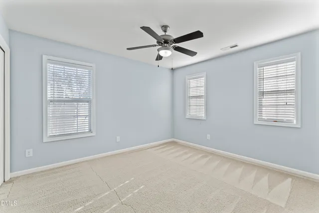an empty room with a chandelier fan and windows