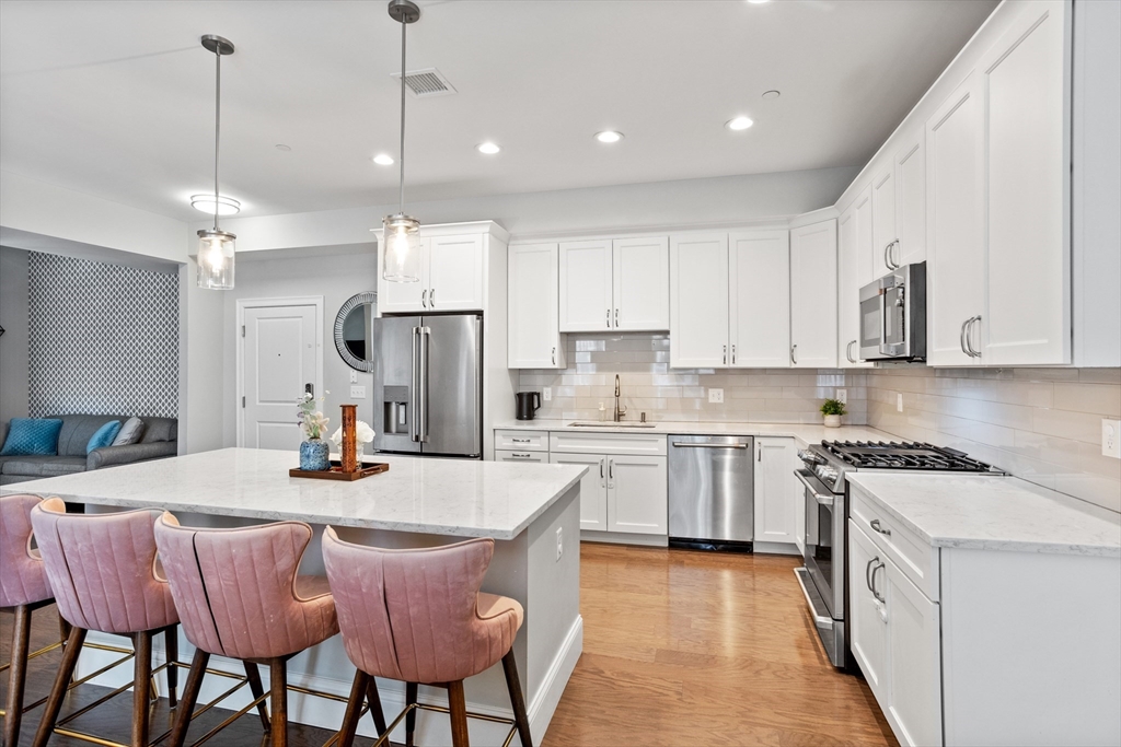 8 Sanborn Street, Unit 2012 Reading, MA 01867 - Photo 10 of 36 a kitchen with stainless steel appliances kitchen island granite countertop a sink a stove a refrigerator and white cabinets with wooden floor