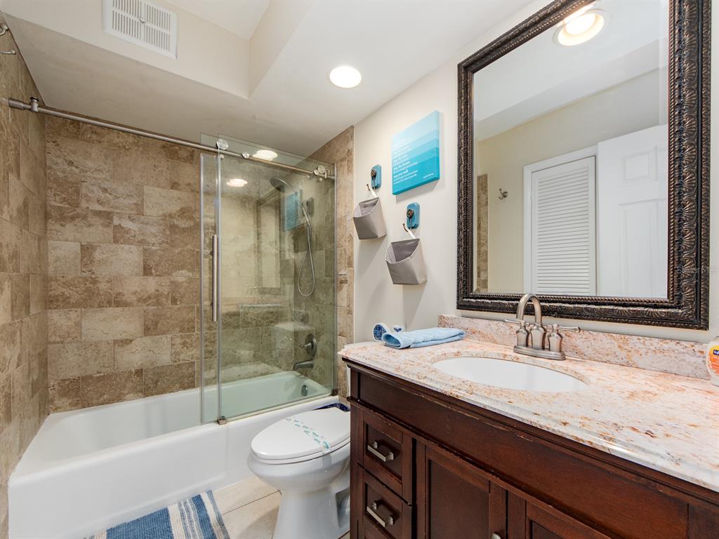 2406 Gulf Boulevard, Unit 204 Indian Rocks Beach, FL 33785 - Photo 24 of 39 a bathroom with a granite countertop sink a toilet a mirror a bathtub and shower