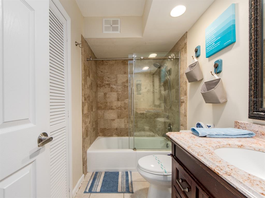 2406 Gulf Boulevard, Unit 204 Indian Rocks Beach, FL 33785 - Photo 25 of 39 a bathroom with a granite countertop sink a toilet a mirror a bathtub and shower