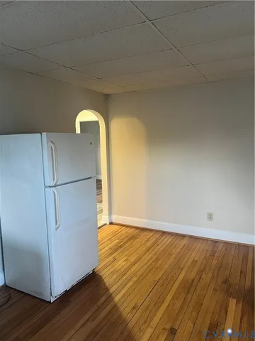 a view of a refrigerator in kitchen and an empty room with wooden floor