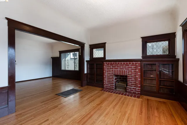 a view of an empty room with wooden floor fireplace and a window