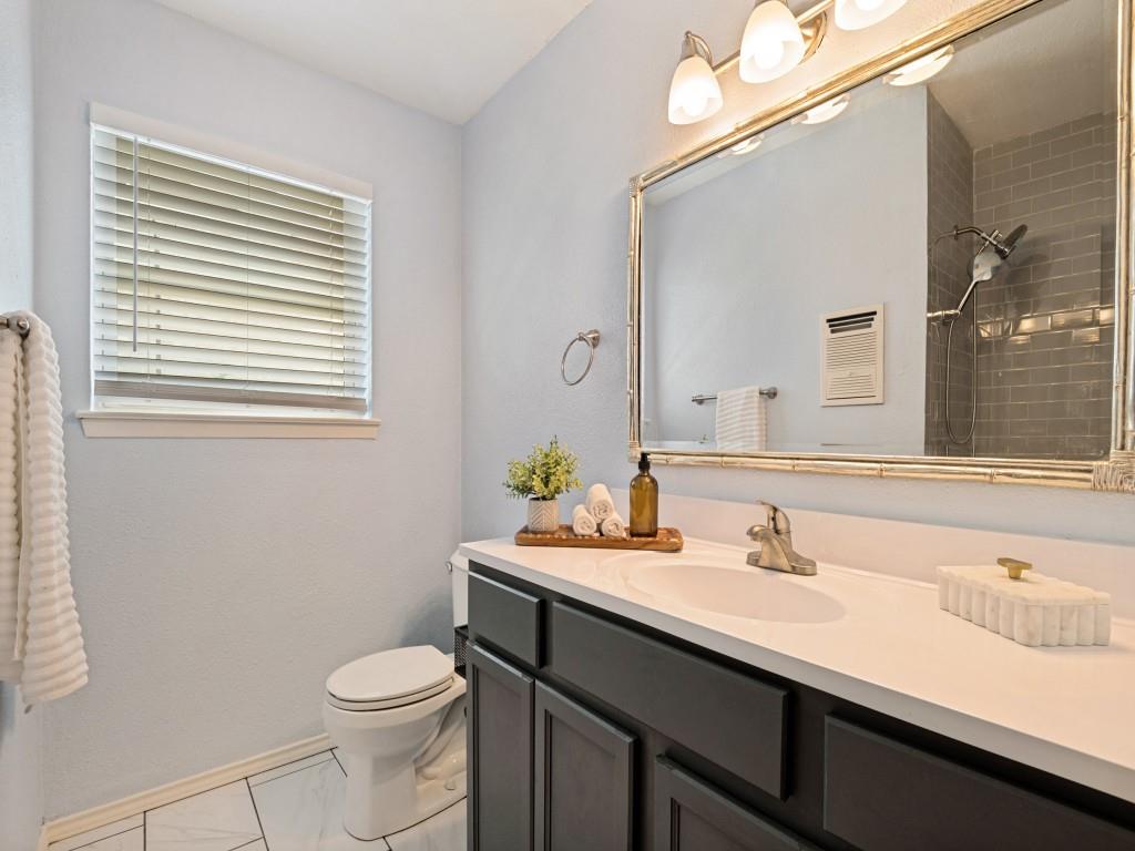 1405 Rambler Road Arlington, TX 76014 - Photo 21 of 26 Bathroom featuring a dark wood-finish vanity with a white countertop, a large framed mirror, and a shower with gray subway tile