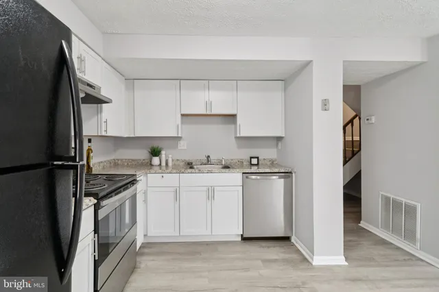 a kitchen with stainless steel appliances granite countertop a refrigerator a stove a sink and white cabinets with wooden floor