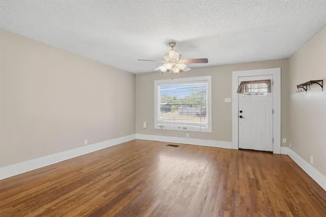 an empty room with wooden floor chandelier fan and windows