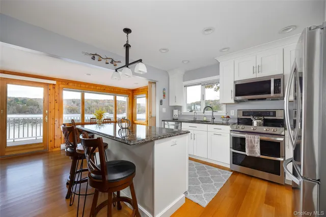 a kitchen with stainless steel appliances kitchen island granite countertop a refrigerator a oven a stove and a dining table with wooden floor