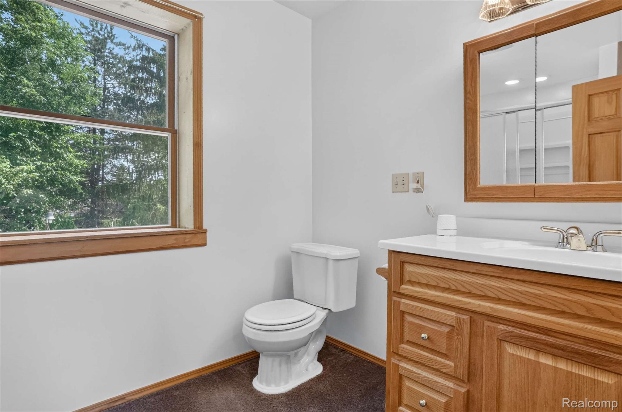 1437 East Cook Road Grand Blanc, MI 48439 - Photo 64 of 69 Bathroom featuring a wood-framed window, a white toilet, and a vanity with wood-finish cabinetry, a white countertop, and a mirrored medicine cabinet