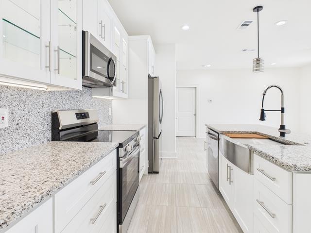 511 Richardson Street Athens, TX 75751 - Photo 12 of 40 Kitchen featuring stainless steel appliances, white cabinetry, light stone countertops, decorative light fixtures, and an island with sink