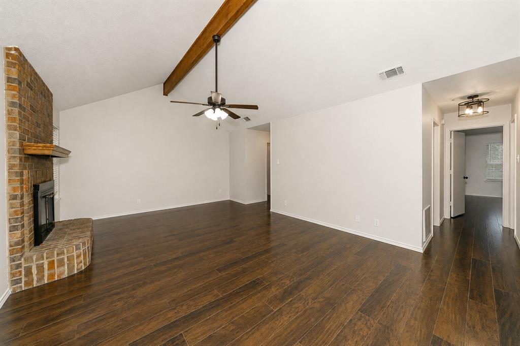 1001 Rosebud Drive Azle, TX 76020 - Photo 10 of 36 Spacious living area featuring high vaulted ceilings with exposed wood beams, a brick fireplace with a hearth and wood mantle, dark wood-finish flooring, and a ceiling fan with integrated lighting