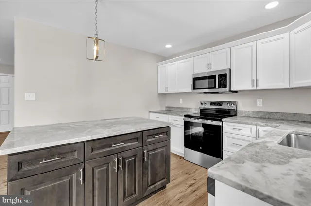 a kitchen with granite countertop a sink dishwasher a stove and a microwave oven with wooden floor