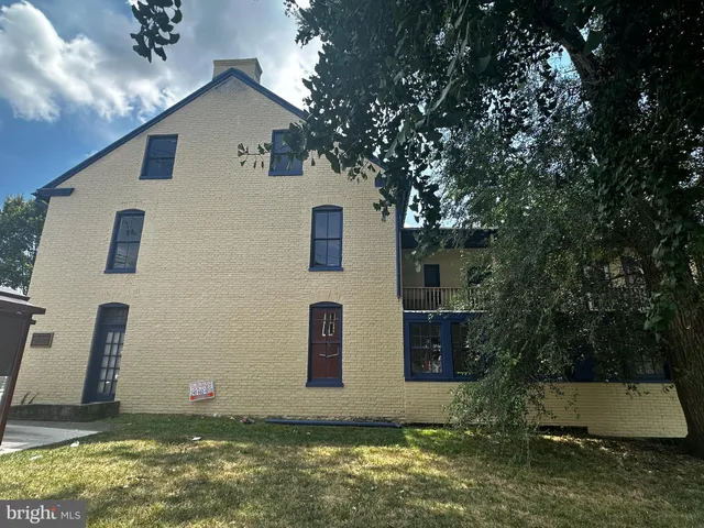 a view of a white house next to a yard with large trees