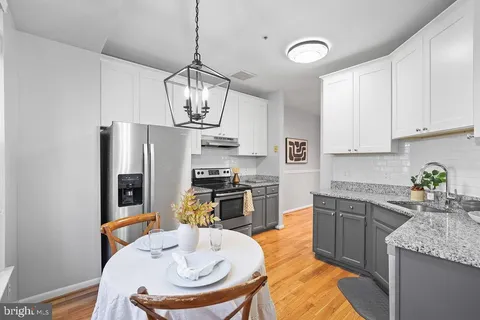 a kitchen with stainless steel appliances granite countertop a sink a stove a refrigerator a dining table and chairs with wooden floor