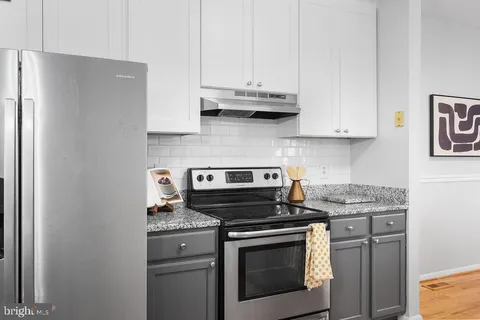 a kitchen with stainless steel appliances granite countertop white cabinets and a stove a refrigerator with white cabinets