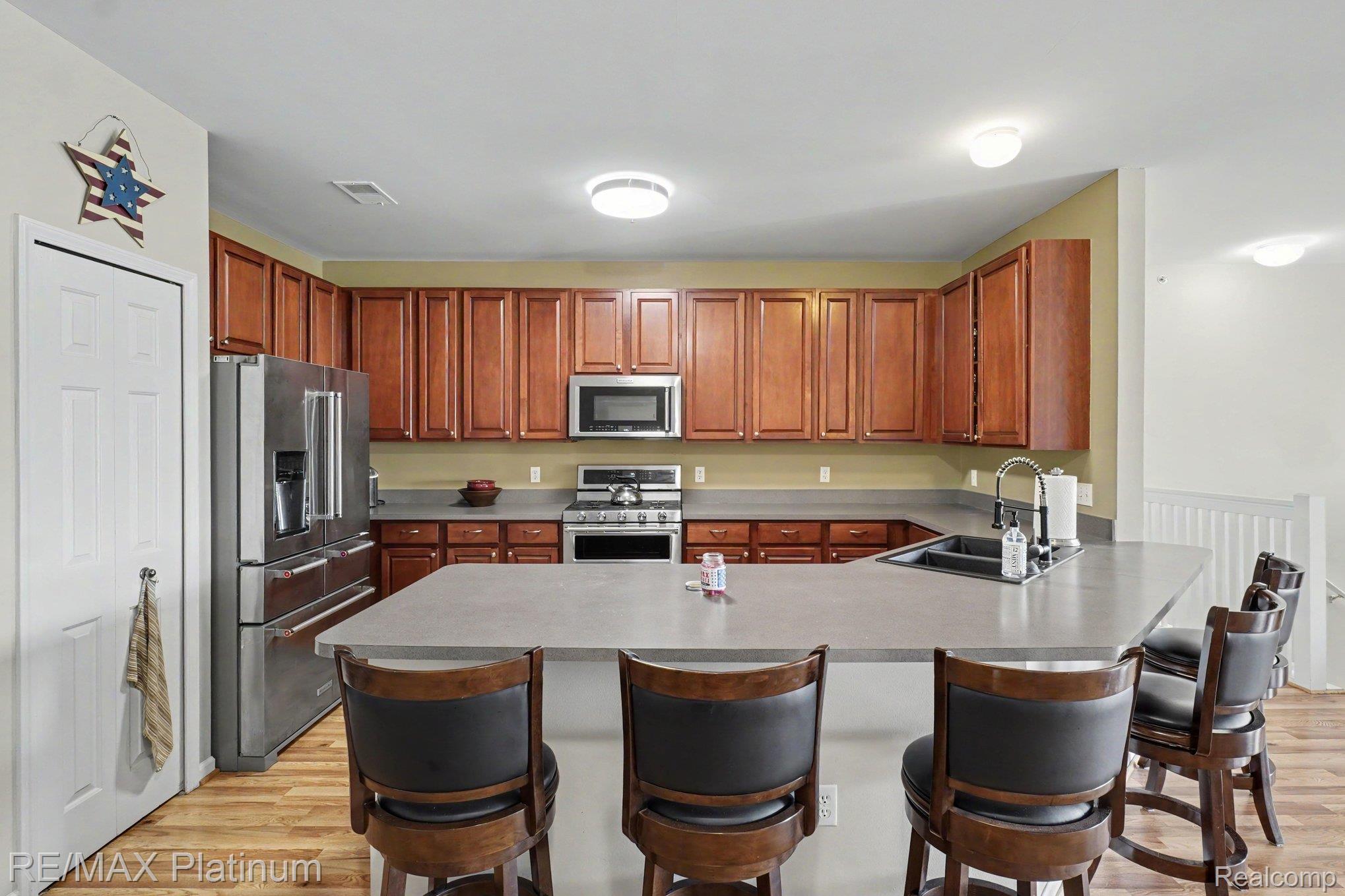 10217 Crossview Trail Howell, MI 48855 - Photo 12 of 26 Kitchen featuring L-shaped counter seating, wood-finish flooring, stainless steel appliances, and abundant cabinet storage