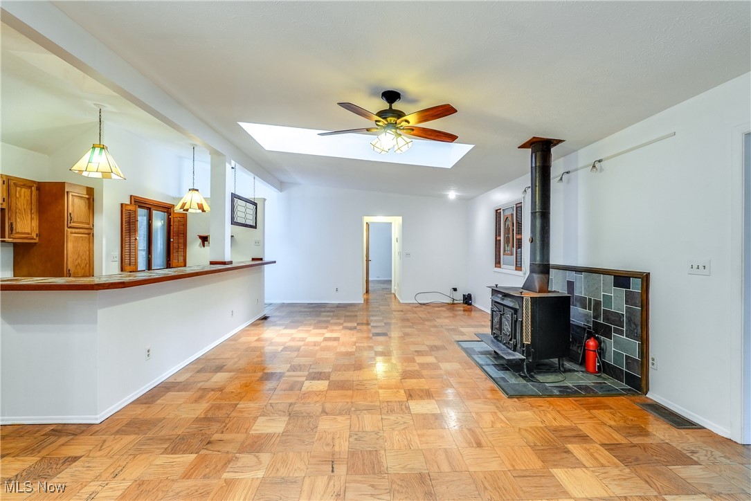 10461 Wye Road Chesterland, OH 44026 - Photo 25 of 50 Unfurnished living room with a wood stove, a ceiling fan, visible vents, a skylight, and baseboards