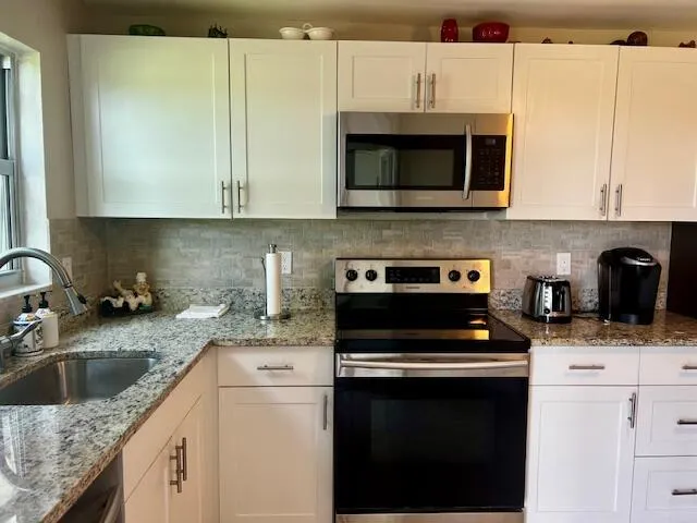 a kitchen with stainless steel appliances granite countertop a refrigerator a stove a sink and a microwave