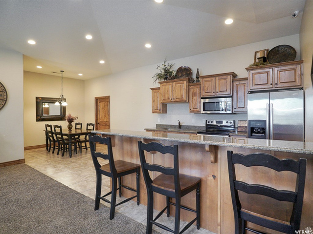 905 South Main Street, Unit G Layton, UT 84041 - Photo 31 of 36 Kitchen featuring dark stone counters, appliances with stainless steel finishes, a kitchen bar, decorative light fixtures, and brown cabinets