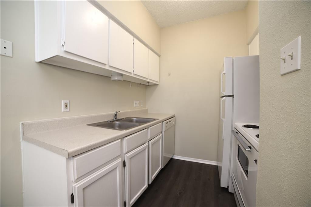 2604 Salado Street, Unit 103 Austin, TX 78705 - Photo 5 of 6 Kitchen featuring white cabinets, white appliances, light countertops, dark wood-type flooring, and a textured ceiling
