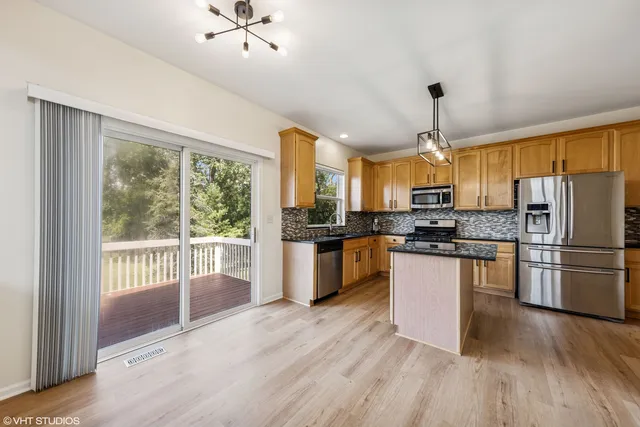 a kitchen with stainless steel appliances kitchen island granite countertop a refrigerator a sink dishwasher a stove and a dining table with wooden floor