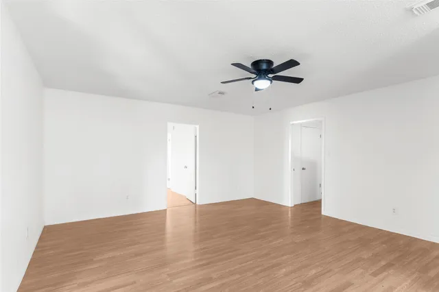 an empty room with wooden floor and a ceiling fan
