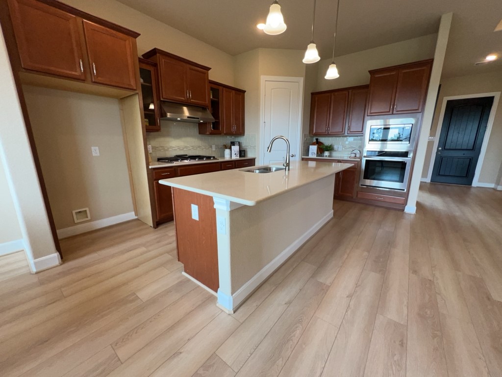 5602 Caracara Street Manvel, TX 77578 - Photo 9 of 27 a large kitchen with stainless steel appliances a large counter top a stove a sink dishwasher and a refrigerator with wooden floor