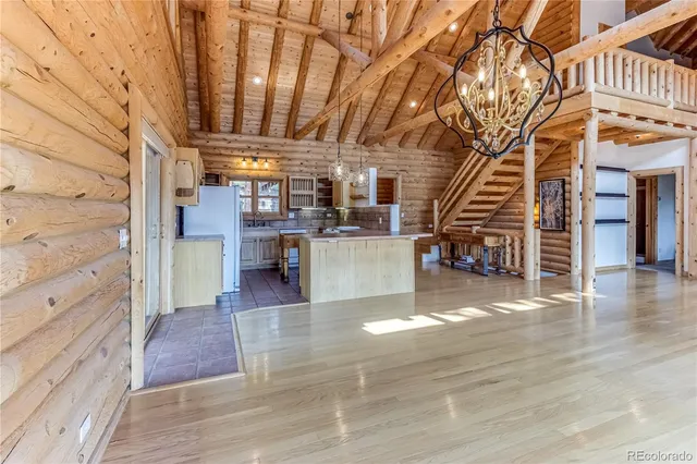 an empty room with wooden floor and way to kitchen