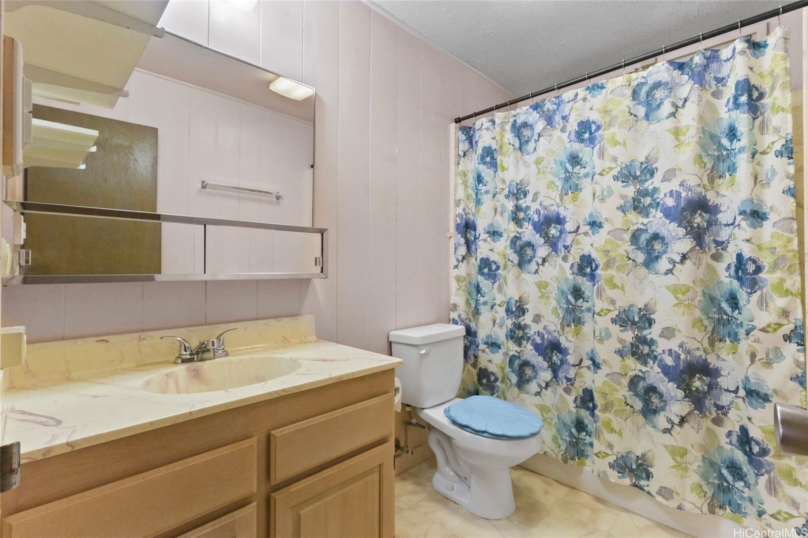 94-341 Kahuanani Street Waipahu, HI 96797 - Photo 14 of 24 a bathroom with a granite countertop toilet a sink a mirror and a shower curtain