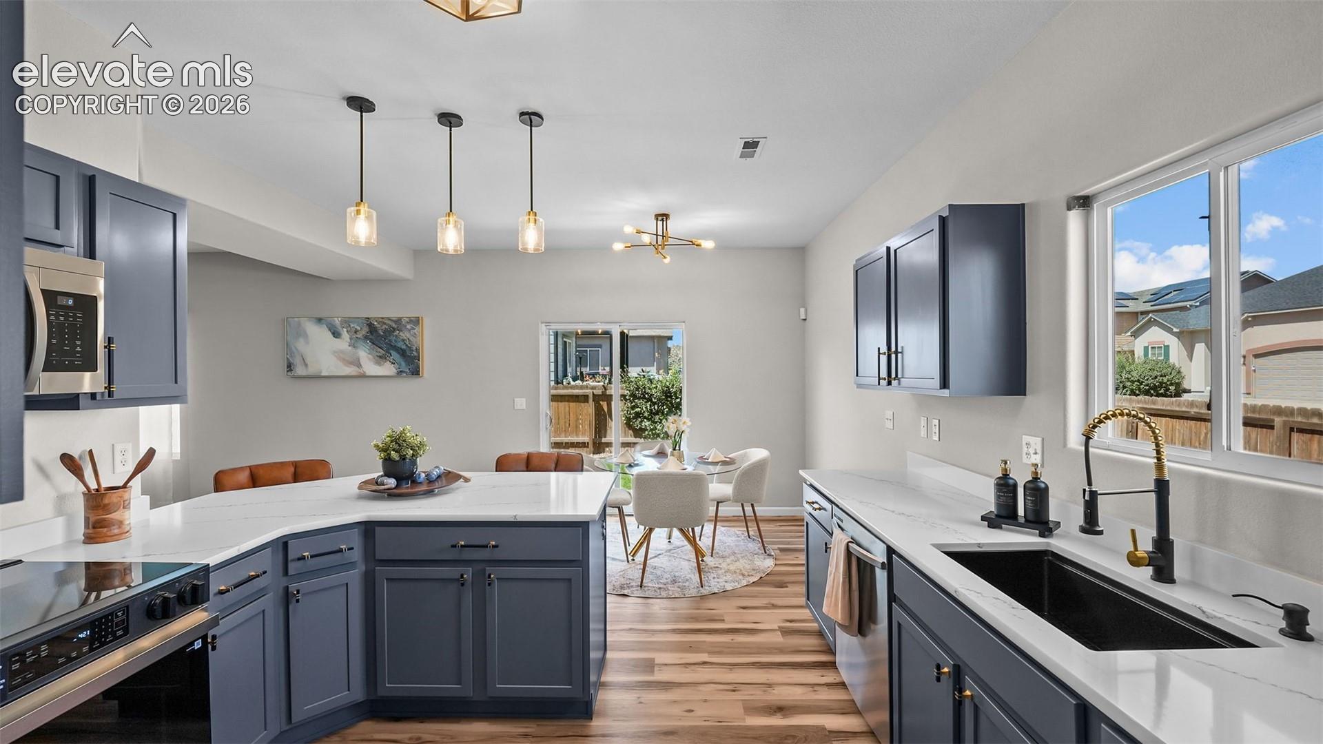 2044 Reed Grass Way Colorado Springs, CO 80915 - Photo 12 of 47 Kitchen featuring dark blue cabinetry, white countertops, stainless steel appliances, wood-finish flooring, and pendant lighting