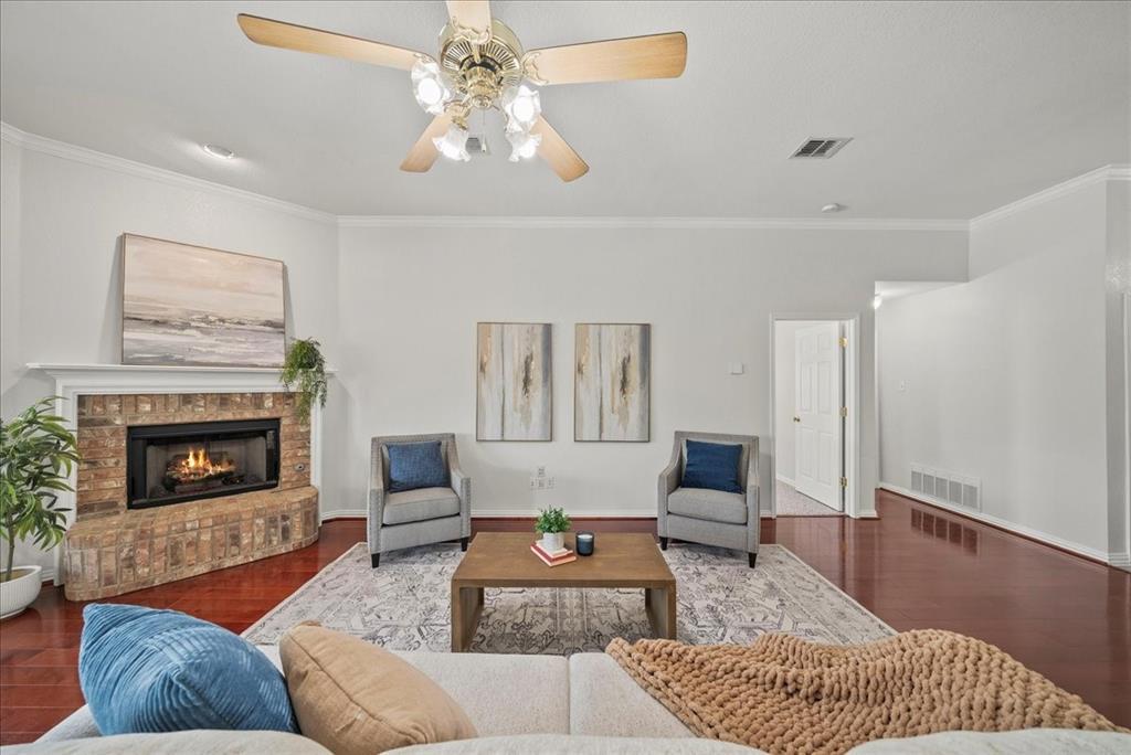 Living room featuring crown molding, dark wood finished floors, a brick fireplace, and a ceiling fan