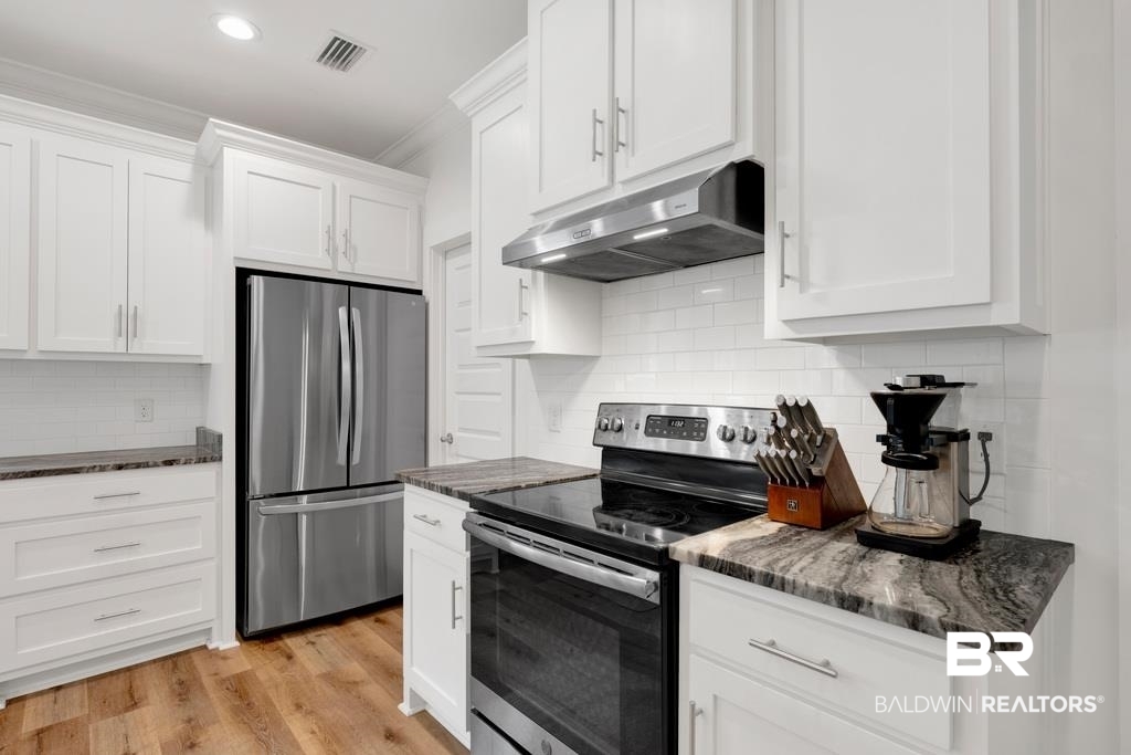 379 Pecan Ridge Boulevard Fairhope, AL 36532 - Photo 7 of 21 Contemporary kitchen featuring white shaker cabinetry, stainless steel appliances, patterned countertops, a white subway tile backsplash, and wood-finish flooring