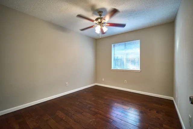 a view of an empty room with wooden floor and a ceiling fan