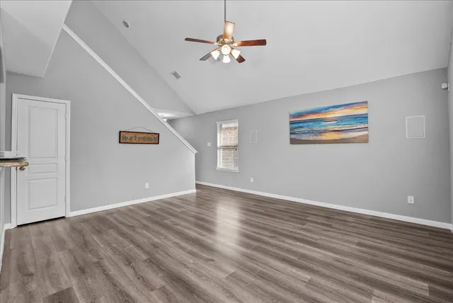 an empty room with wooden floor chandelier fan and windows