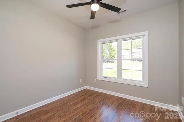 an empty room with wooden floor ceiling fan and windows