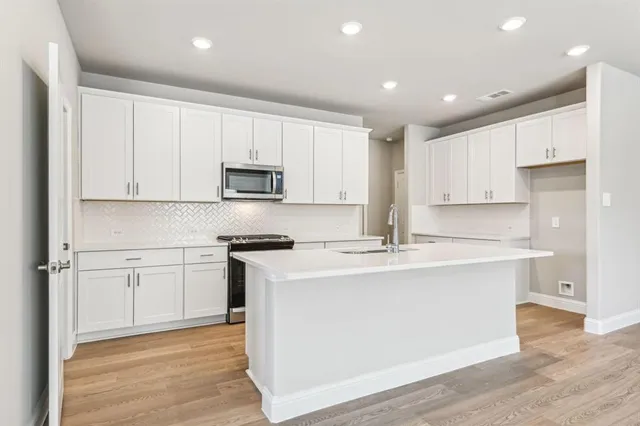 a kitchen with stainless steel appliances granite countertop a stove top oven a sink and white cabinets