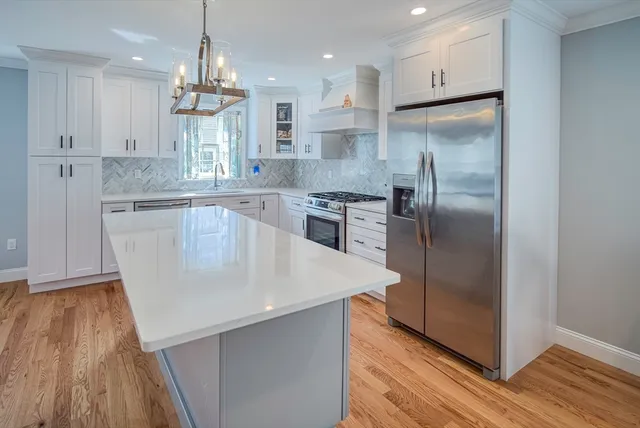 a kitchen with stainless steel appliances granite countertop a refrigerator a sink dishwasher a stove and white cabinets with wooden floor