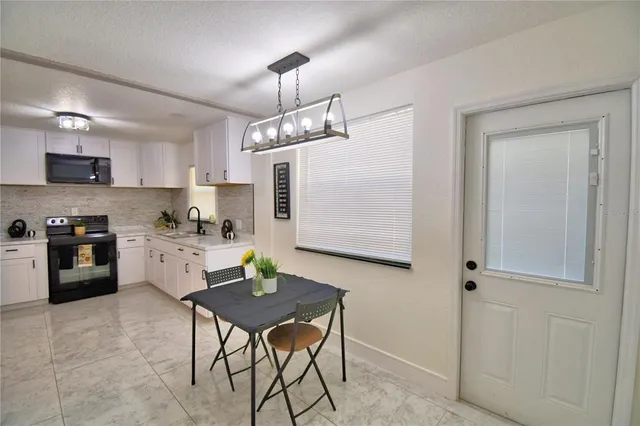 a kitchen with stainless steel appliances granite countertop a stove a sink dishwasher a refrigerator and a dining table with white cabinets