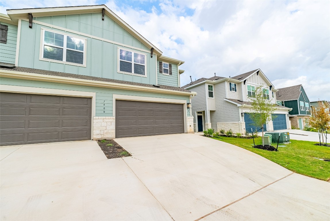 View of front of property featuring board and batten siding, concrete driveway, an attached garage, stone siding, and a residential view