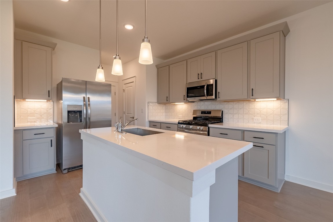 7400 Sparkling Light Drive, Unit A Del Valle, TX 78617 - Photo 6 of 22 Kitchen with appliances with stainless steel finishes, a center island with sink, backsplash, pendant lighting, and light stone countertops