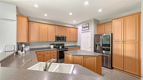 a kitchen with stainless steel appliances granite countertop wooden cabinets a sink dishwasher a stove and a refrigerator with wooden floor