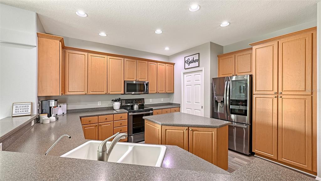 12274 23rd Street East Parrish, FL 34219 - Photo 15 of 64 a kitchen with stainless steel appliances granite countertop a refrigerator a stove a sink a washer dryer and chairs