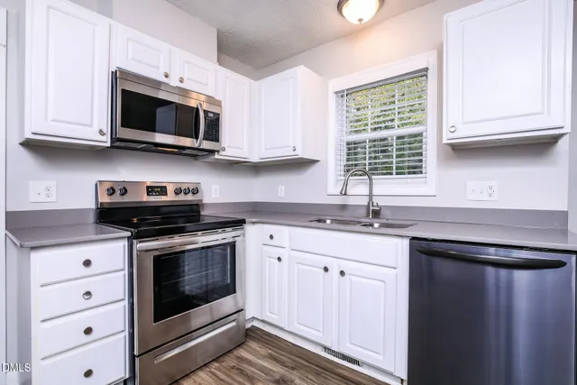a kitchen with stainless steel appliances granite countertop a stove top oven a sink dishwasher a microwave oven and a refrigerator with wooden floors