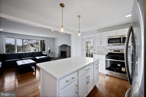 a kitchen with stainless steel appliances kitchen island granite countertop a refrigerator a stove oven a sink dishwasher and white cabinets with wooden floor